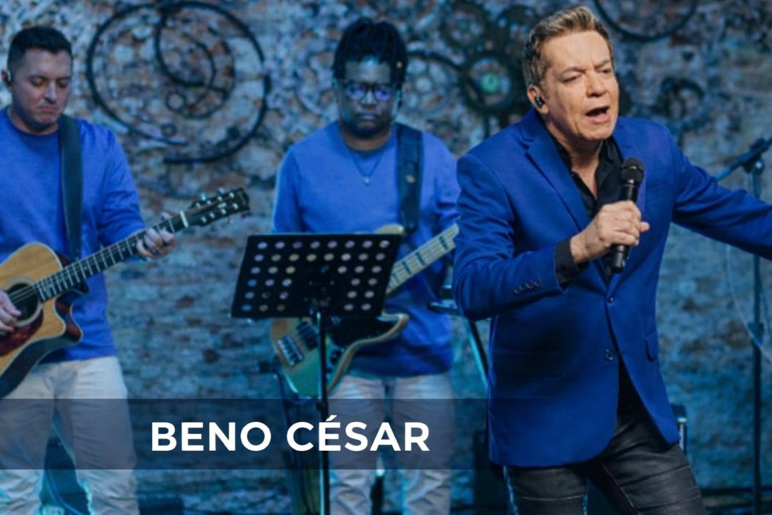 Beno César em apresentação, com microfone na mão.